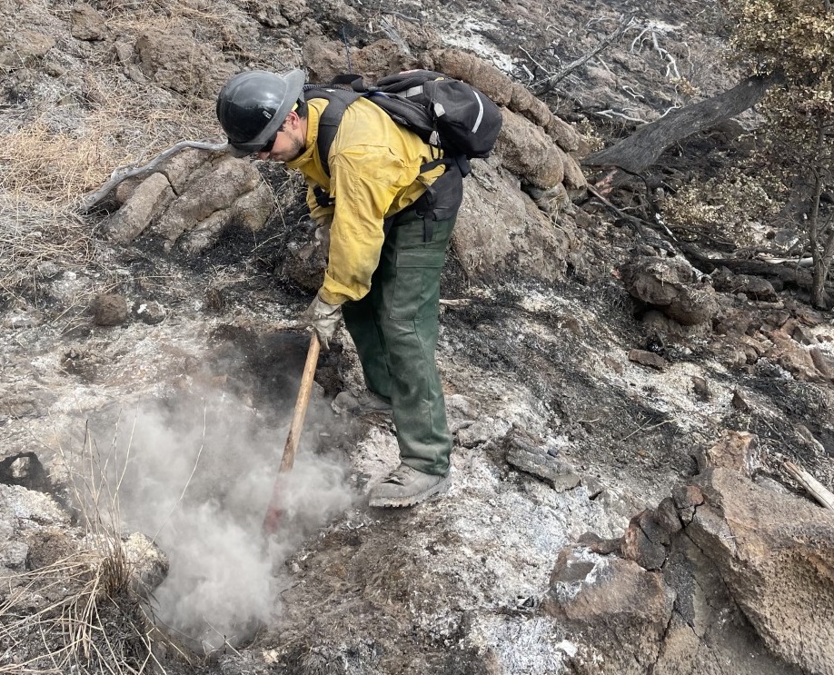 Hawaii Volcanoes NP Wildland Firefighter using handtool to mop up A firefighter in protective gear uses a hand tool to extinguish a smoking hot spot on the ground