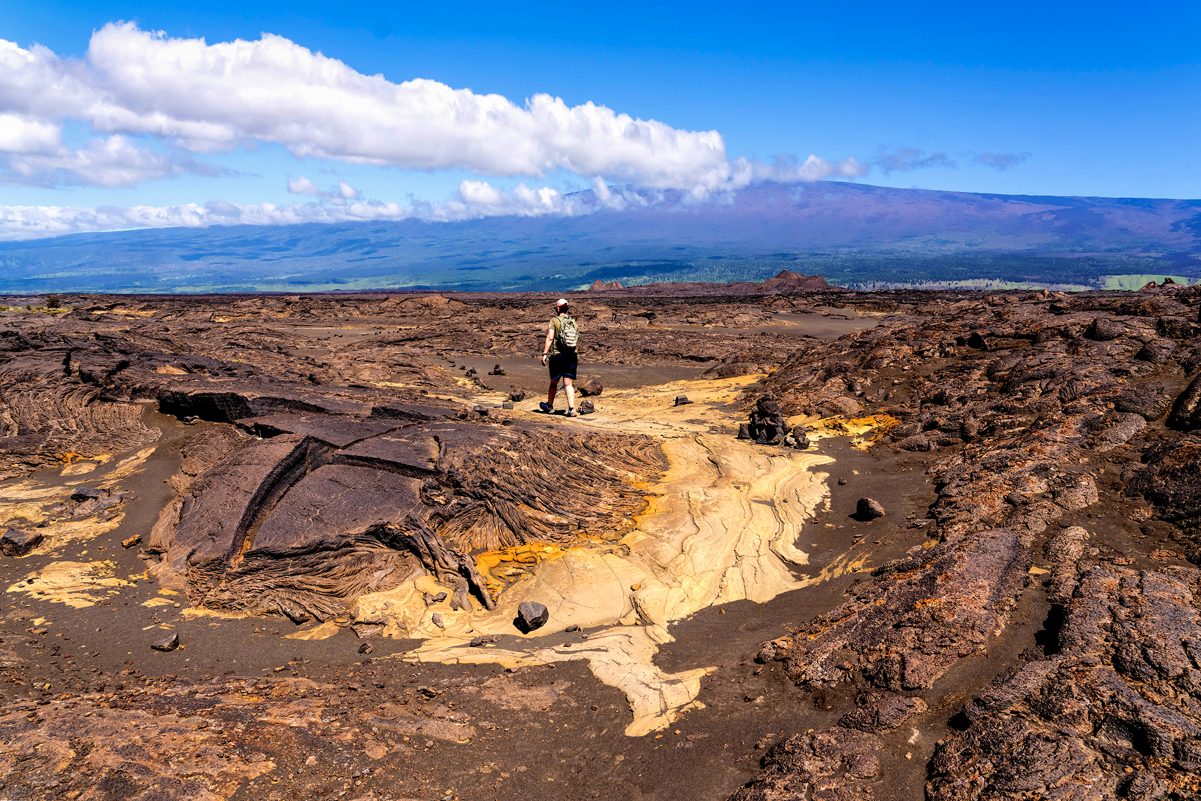A visitor walking in a volcanic desert made of ash and hardened lava flows.