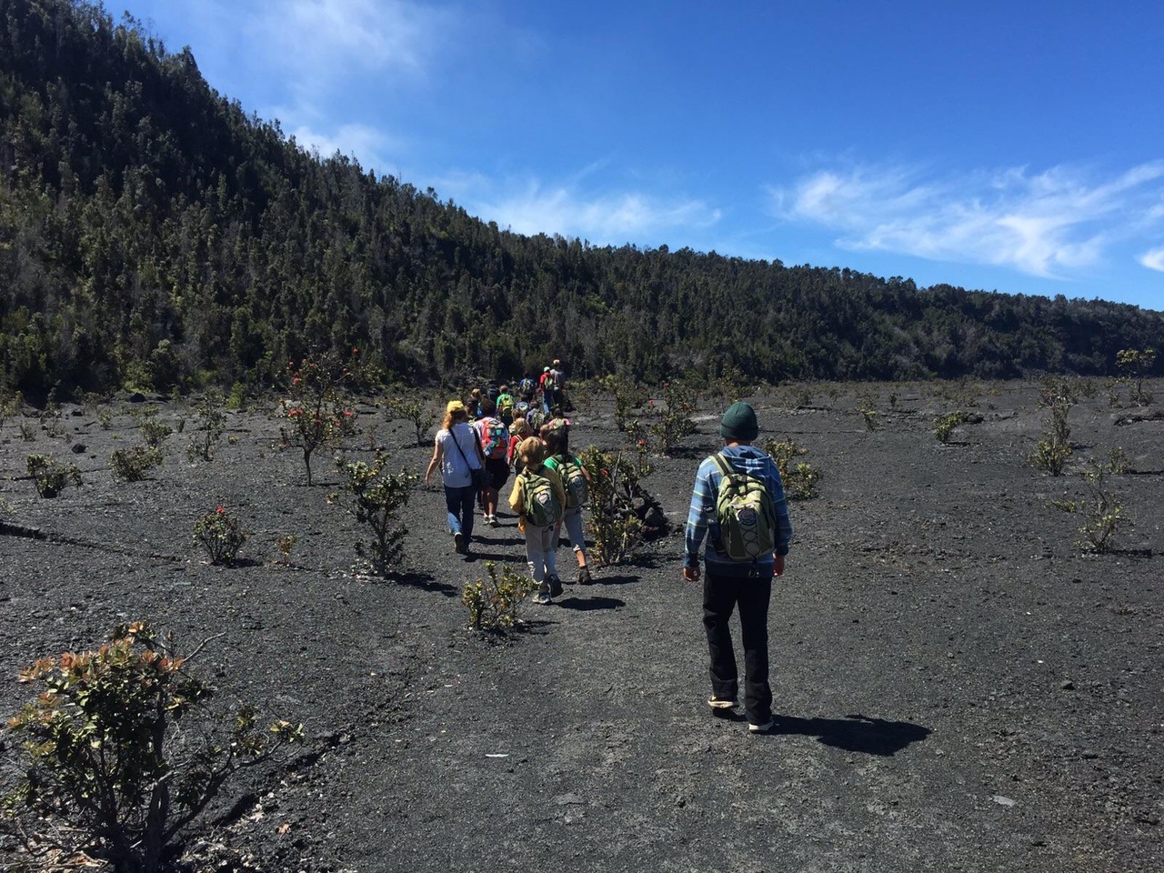 A line of children hike across a caldera floor with steep vegetated cliffs above them