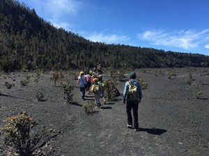 A line of children hike across a caldera floor with steep vegetated cliffs above them