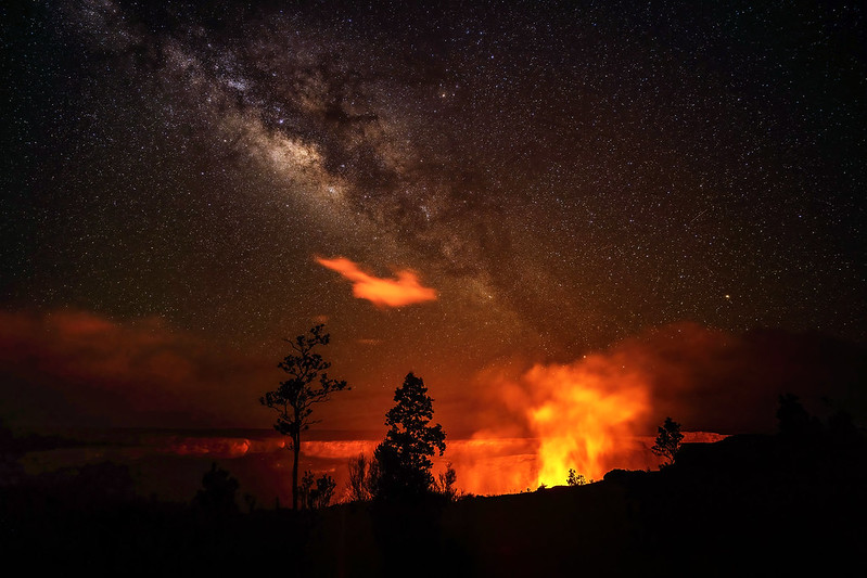 Orange light from inside a deep crater at night with shadows of trees and a multitude of stars.