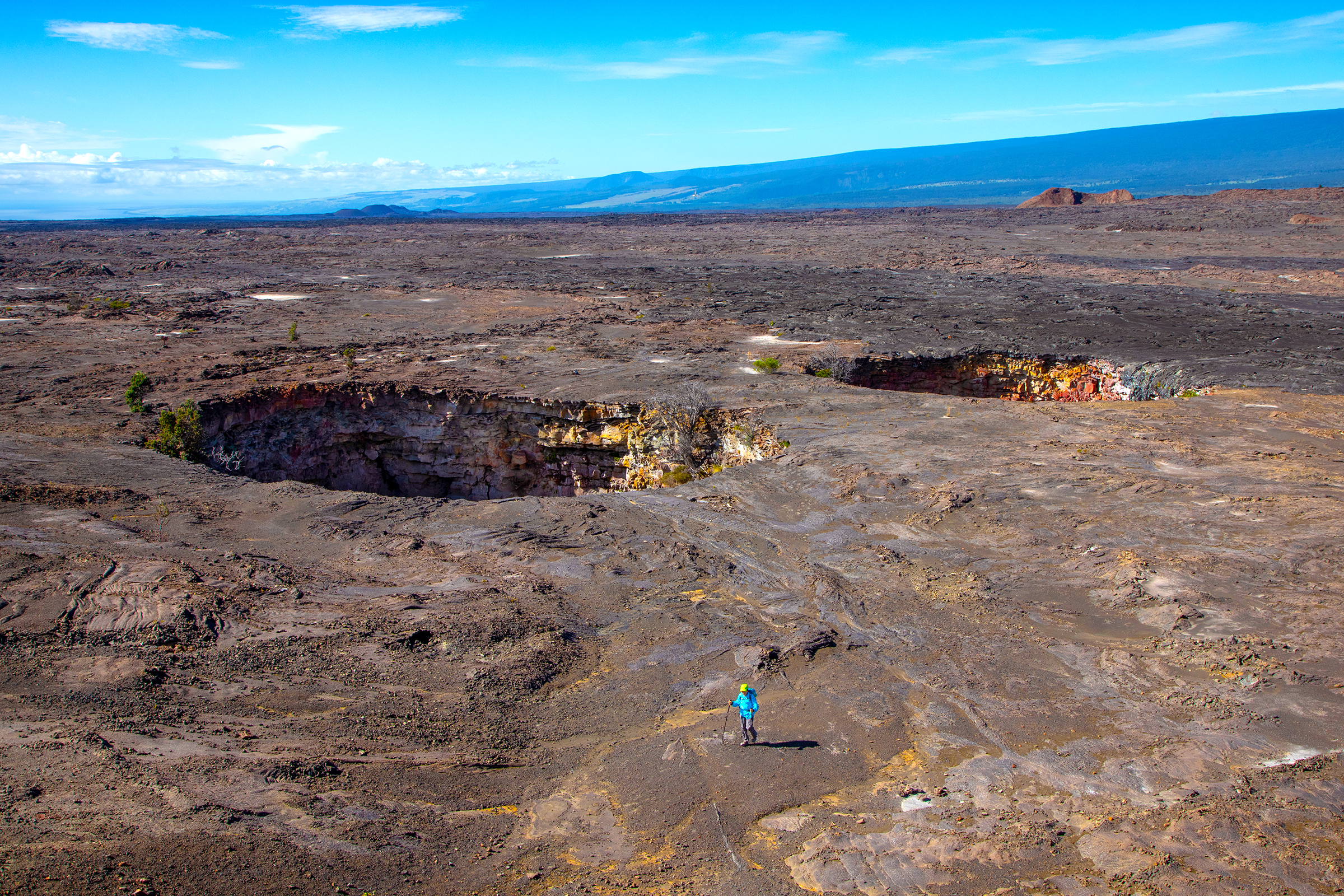 Hiker next to two large craters that are side-by-side. Vast volcanic desert.