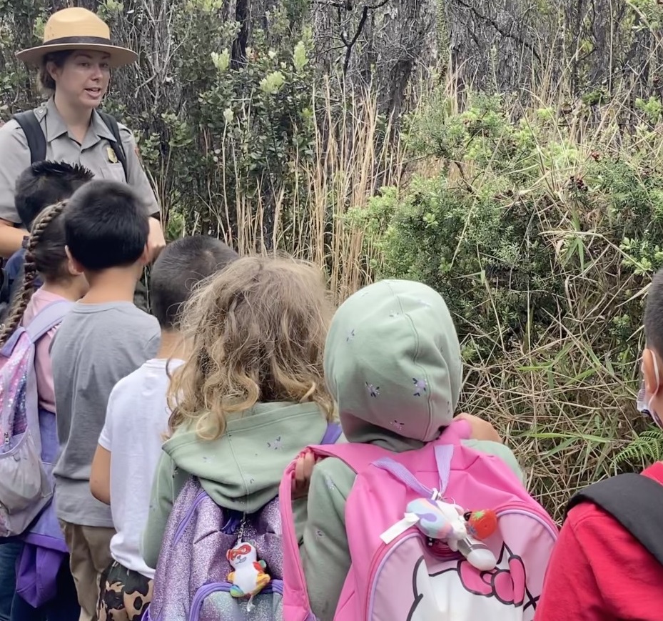 Park Ranger Erin Destin with schoolkkids in the forest A park ranger leads a group of young backpack-wearing school children on a hike near plants