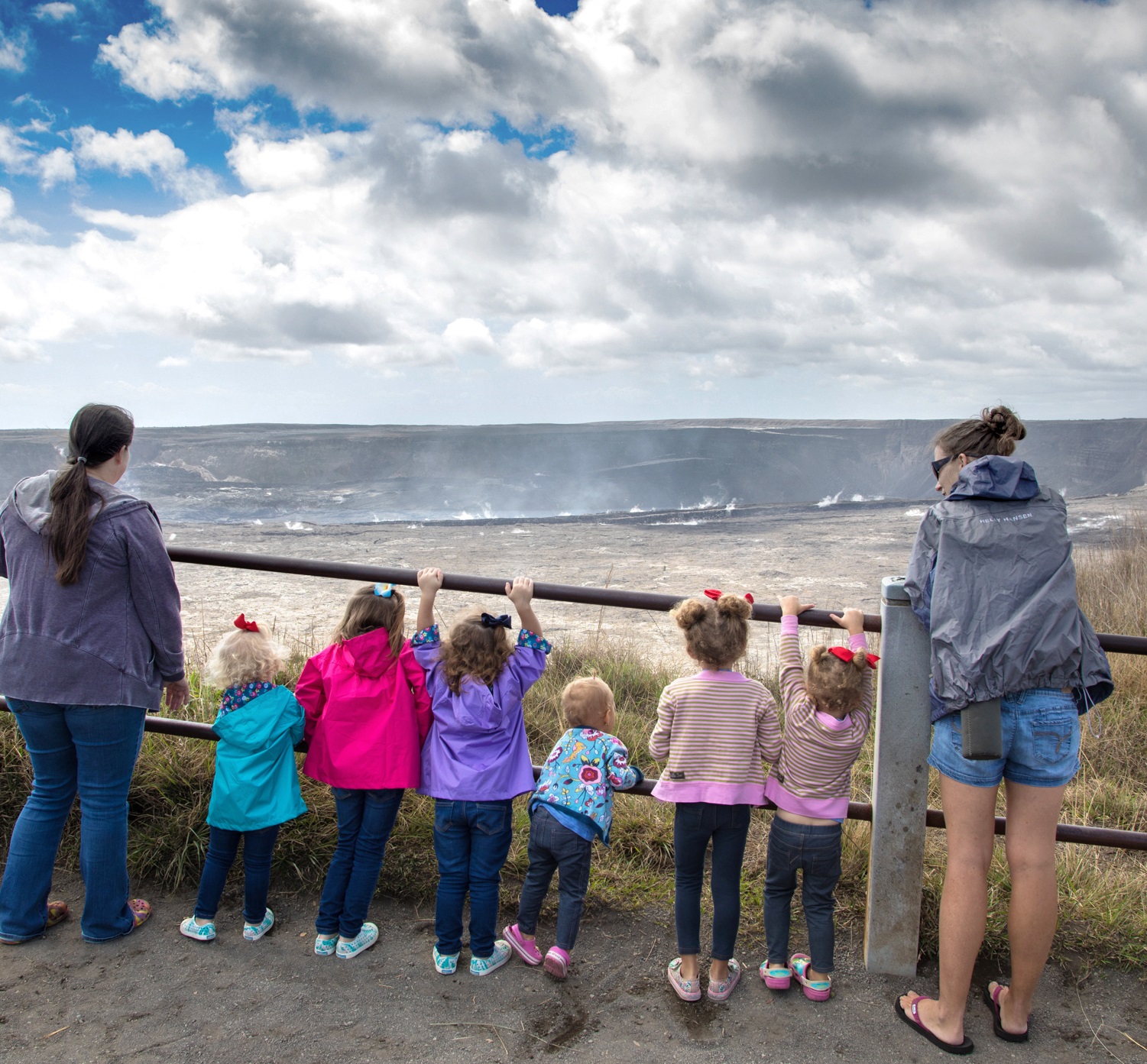 Young children and two adults stand at an overlook on the rim of a steaming volcano