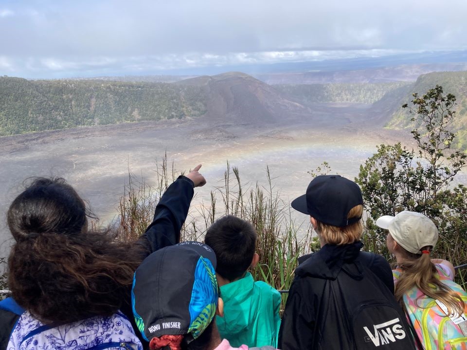 students pointing at rainbow above a crater