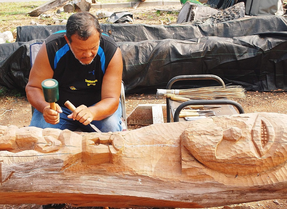 A man carves a wooden statue on the ground