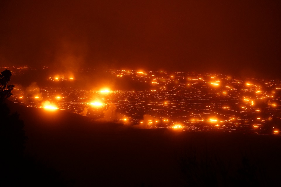 A large volcanic crater filled with red glowing lava at night.