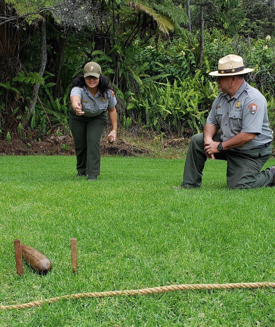 Two rangers demonstrate a Hawaiian game of tossing a wooden club between two stakes in the ground.
