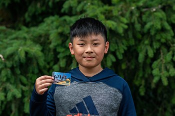 Young boy holding a park pass in front of a background of tree foliage
