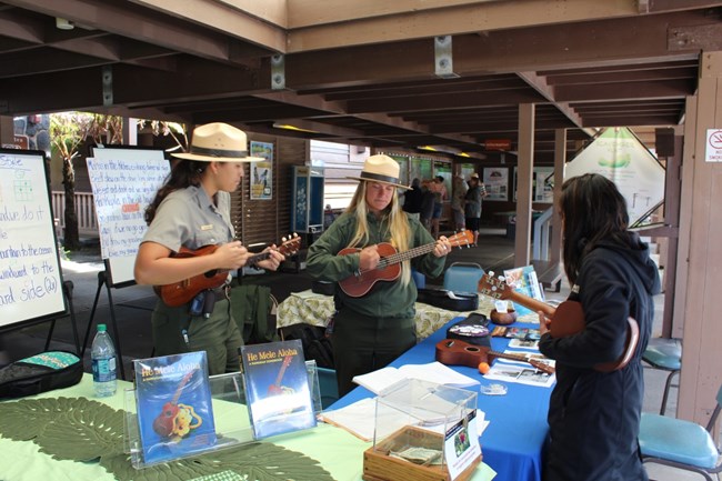 Rangers Shyla (left) and Erica strum ‘ukulele at a ‘Ike Hana No‘eau (Experience the Skillful Work) workshop.