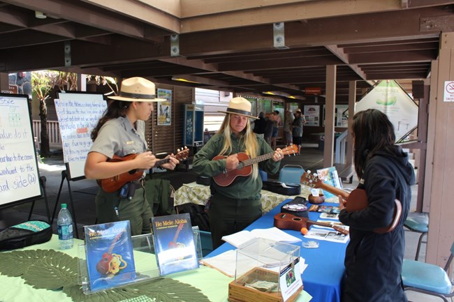 Rangers Shyla (left) and Erica strum ‘ukulele at a ‘Ike Hana No‘eau (Experience the Skillful Work) workshop. Rangers Shyla (left) and Erica strum ‘ukulele at a ‘Ike Hana No‘eau (Experience the Skillful Work) workshop.