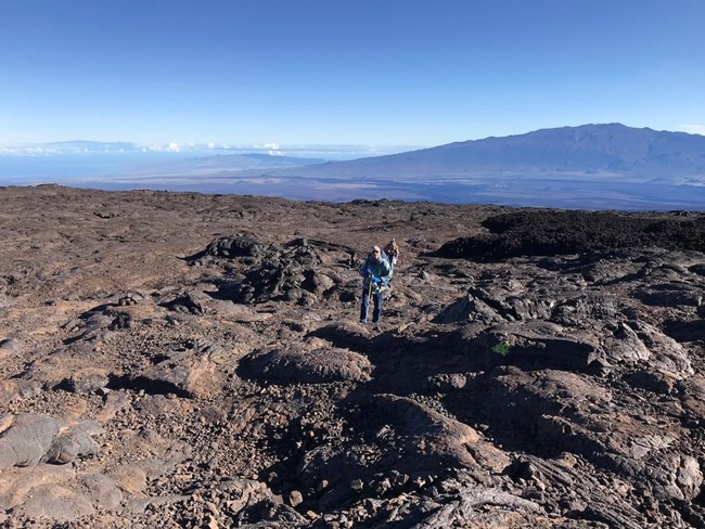 A hiker on a rocky trail through a lava field