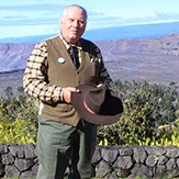 A man stands in old fashioned clothing at the edge of a volcano