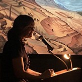 A woman stands at a podium in front of a projection screen