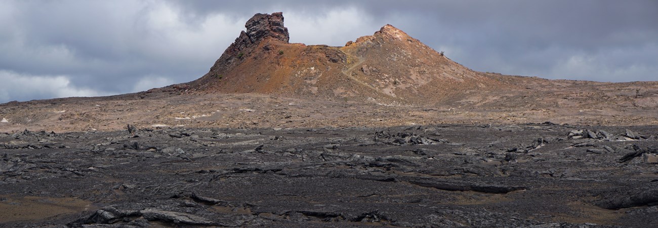 A sunlit cinder cone in a gray volcanic landscape