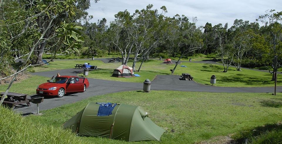 A and open and grassy campground with tents set up and a parked red car