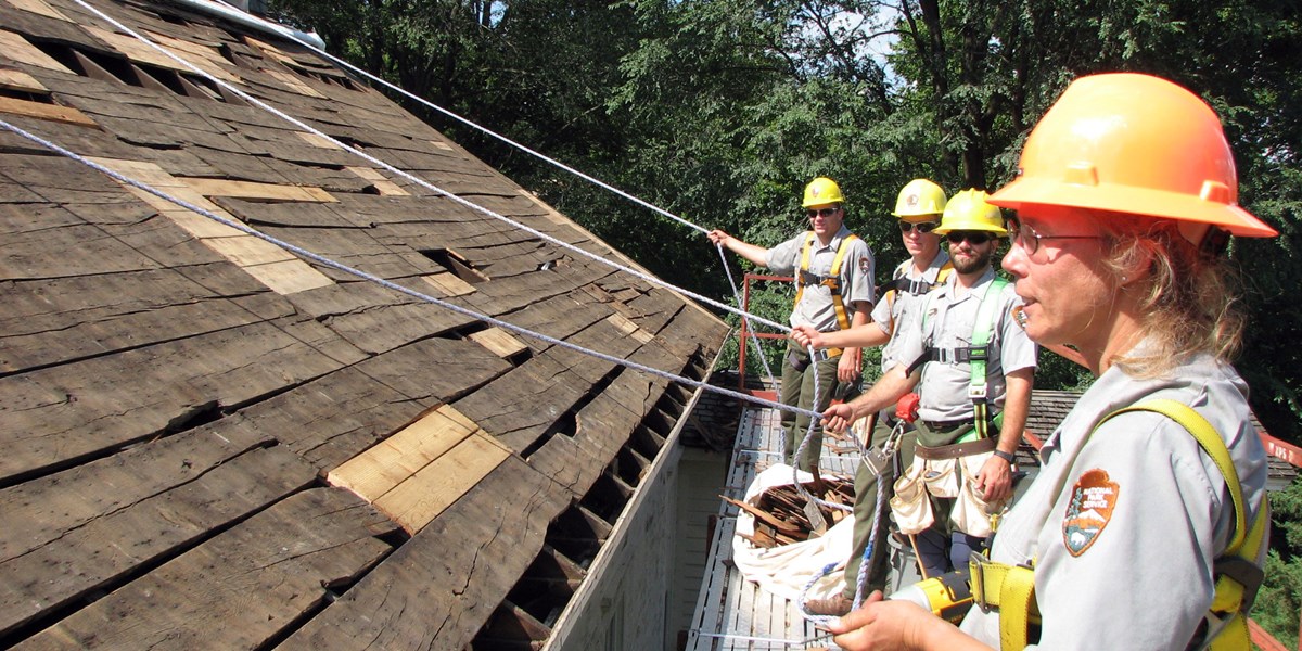 Uniformed workers in hard hats stand on a scaffold for a roofing job. Uniformed workers in hard hats stand on a scaffold for a roofing job.