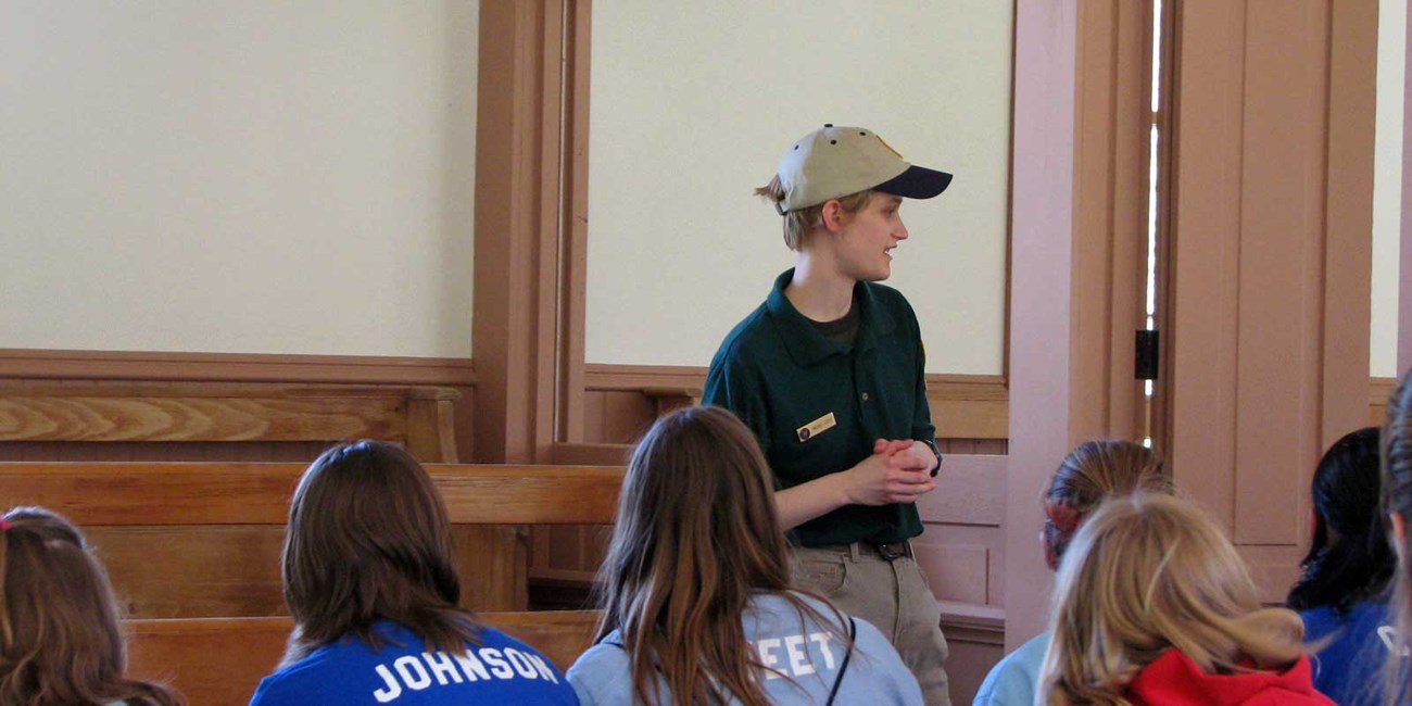 A woman in a volunteer uniform speaks to school children.
