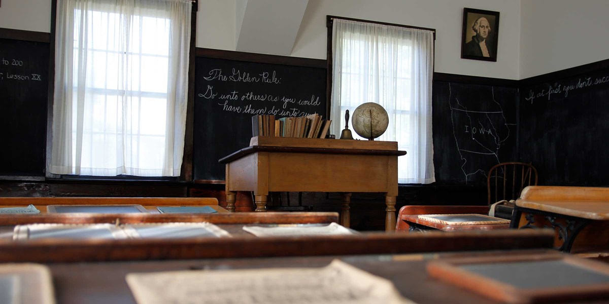 The teacher's desk in a restored 1870s classroom is seen from a pupil's desk. The teacher's desk in a restored 1870s classroom is seen from a pupil's desk.