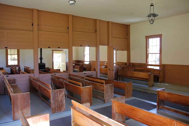Rows of wooden benches fill a room divided by a partition with sliding panels.