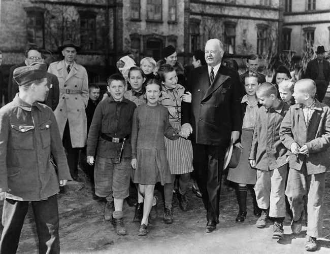 Admiring children surround an elderly Herbert Hoover during a visit to Warsaw.