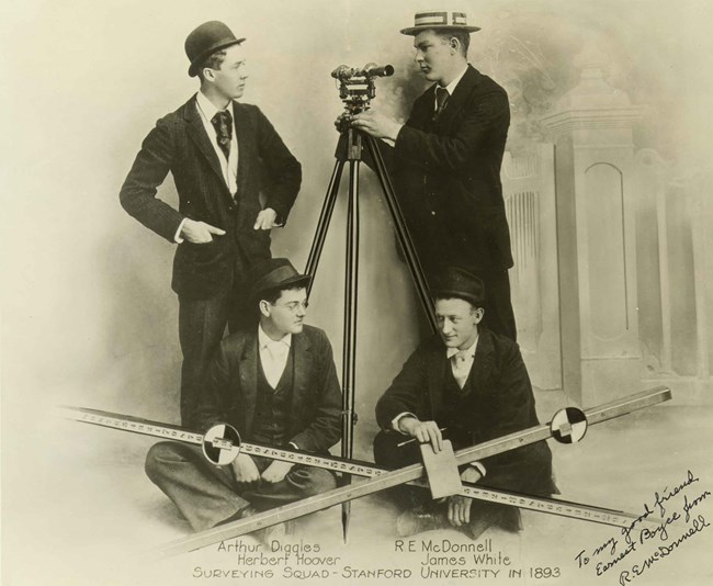 Four young men in 1890s clothes sit with their equipment for a surveying team portrait.