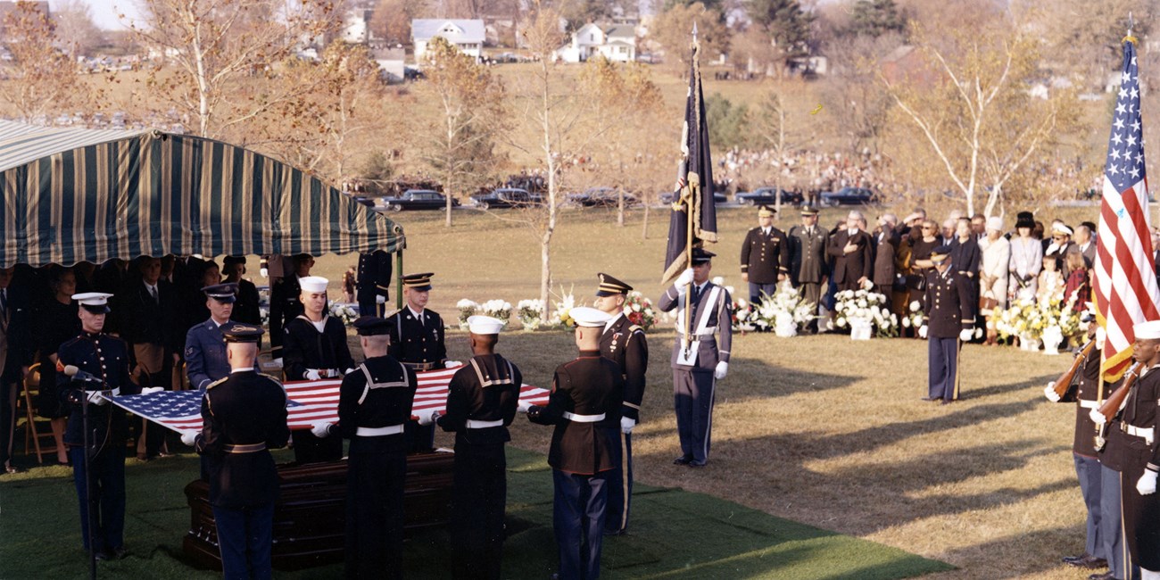 Mourners look on as American servicemen fold a flag over a coffin.