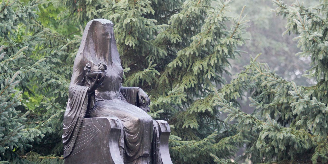 A bronze statue of a seated goddess is displayed in a park.