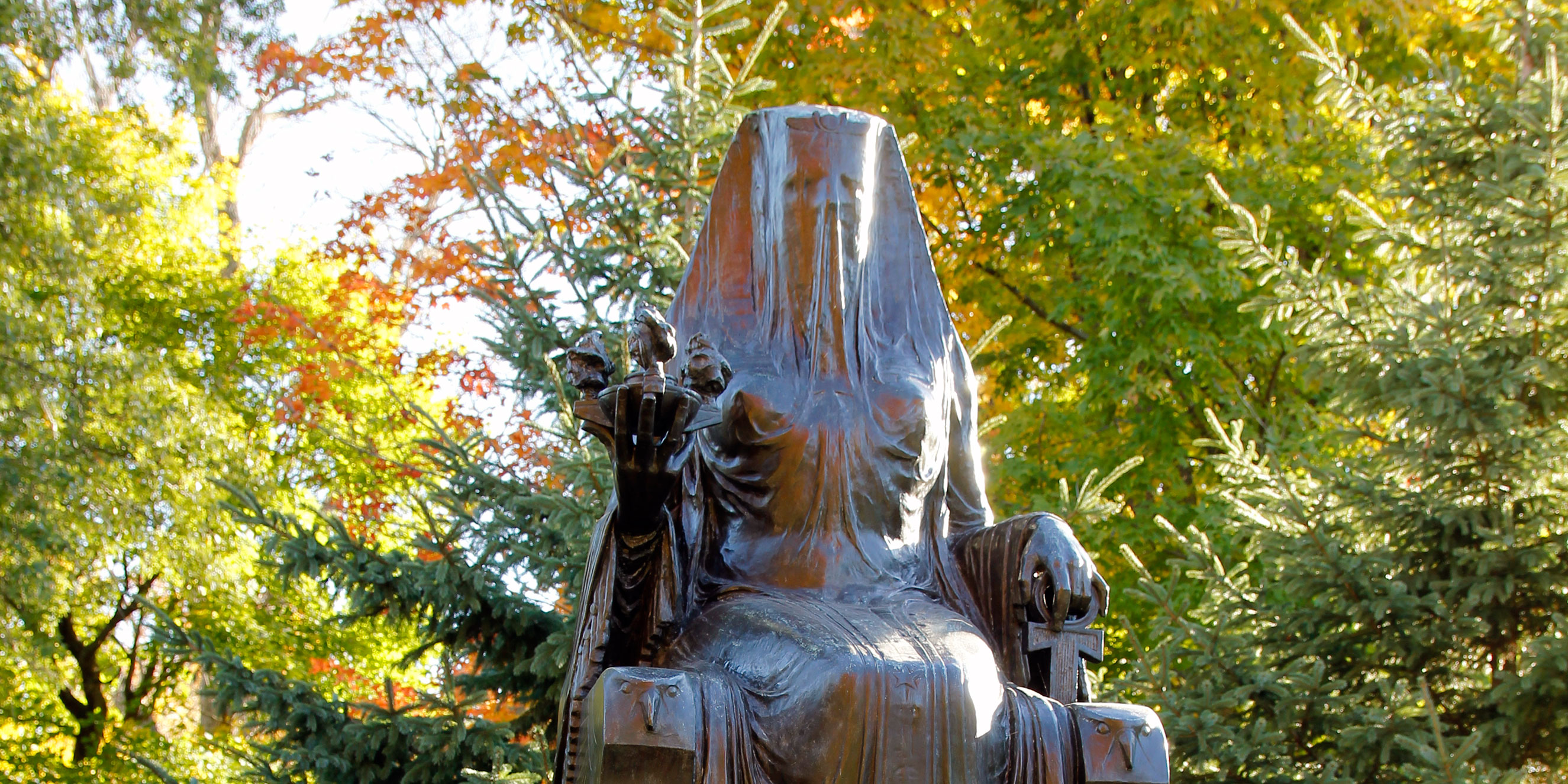 A cast bronze figure of a veiled goddess sits on a throne mounted on a concrete pedestal. A cast bronze figure of a veiled goddess sits on a throne mounted on a concrete pedestal.