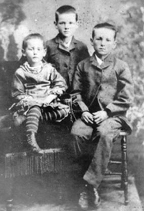Black and white studio photo three seated children, a girl of about seven, a boy of about eight, and another boy of about ten. Black and white studio photo three seated children, a girl of about seven, a boy of about eight, and another boy of about ten.