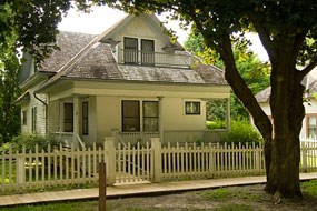 A white two-story house with a porch and picket fence. A white two-story house with a porch and picket fence.