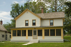 A cream colored two story house with a broad enclosed porch and yellow trim. A cream colored two story house with a broad enclosed porch and yellow trim.