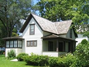 A white house with brown trim surrounded by a green lawn and leafy trees. A white house with brown trim surrounded by a green lawn and leafy trees.
