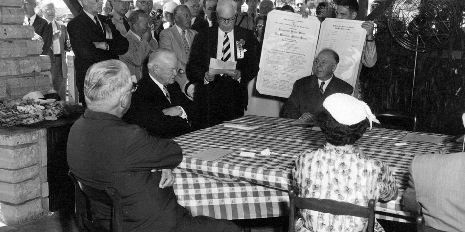 A 1954 photo depicts dignitaries honoring a former president at a picnic shelter. A 1954 photo depicts dignitaries honoring a former president at a picnic shelter.