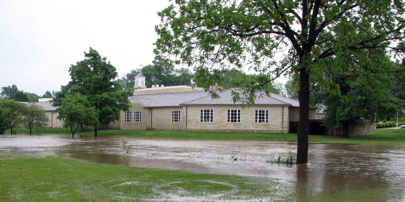 Waters from a flooding creek swamp trees and approach a museum.