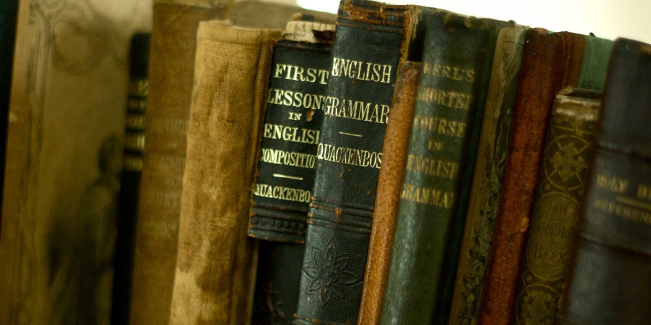 Antique bound textbooks and readers line a shelf in a historic school.