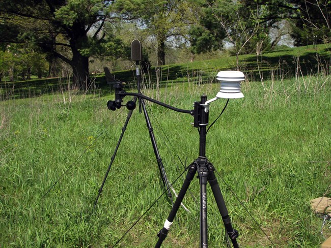 A portable weather station and sound monitoring instrument set up in a field.