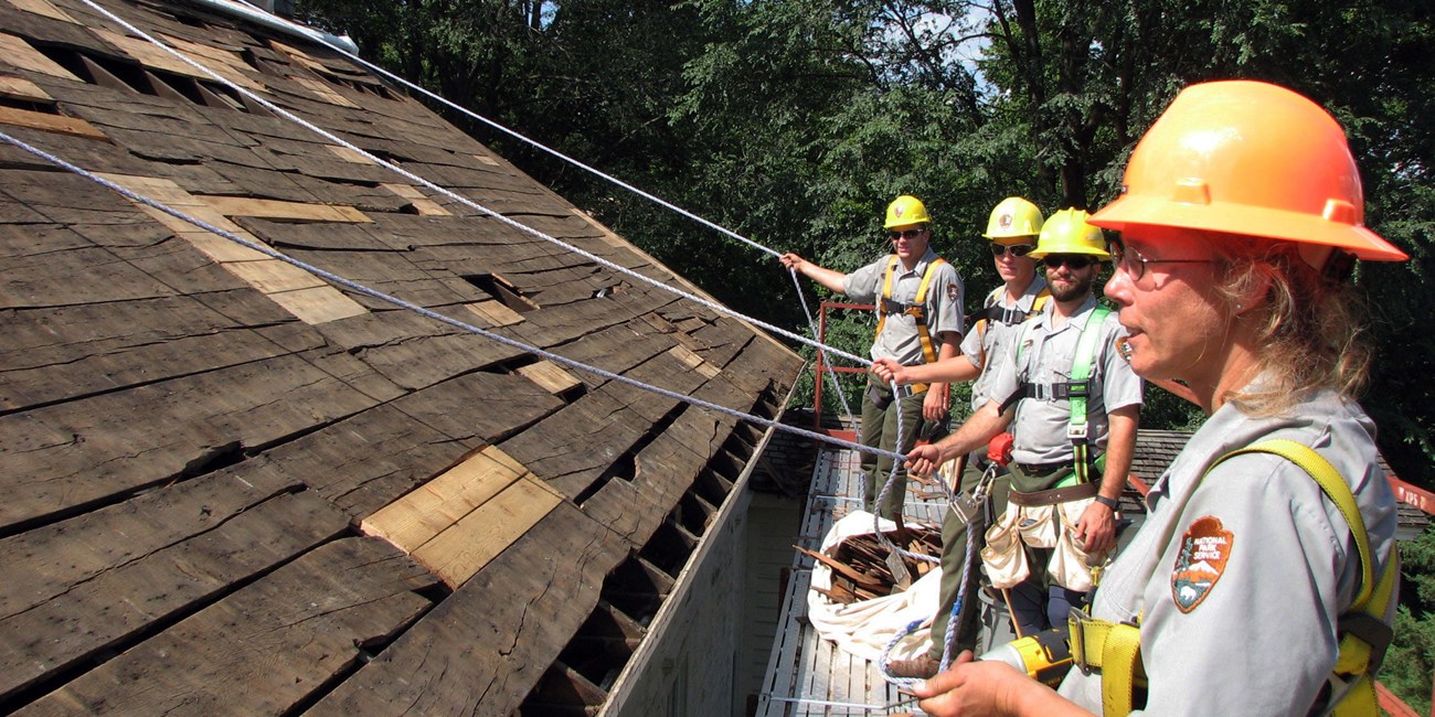 Four workers in orange hardhats re-roof a building from a scaffold.