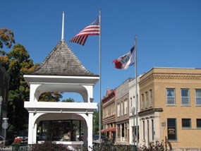 A white gazebo with flags in front of historic commercial downtown block. A white gazebo with flags in front of historic commercial downtown block.