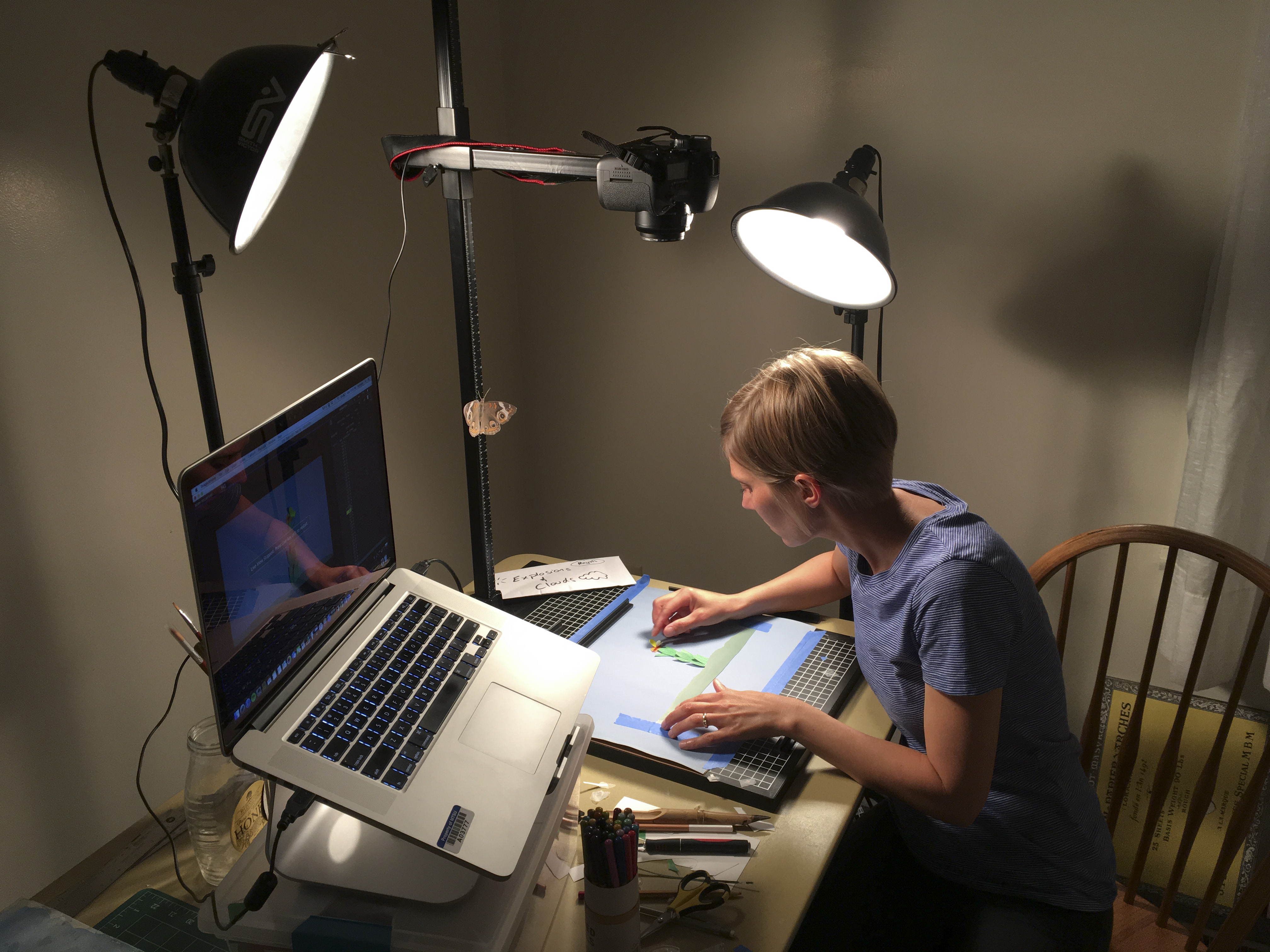 A woman works at a table with a computer and art boards.