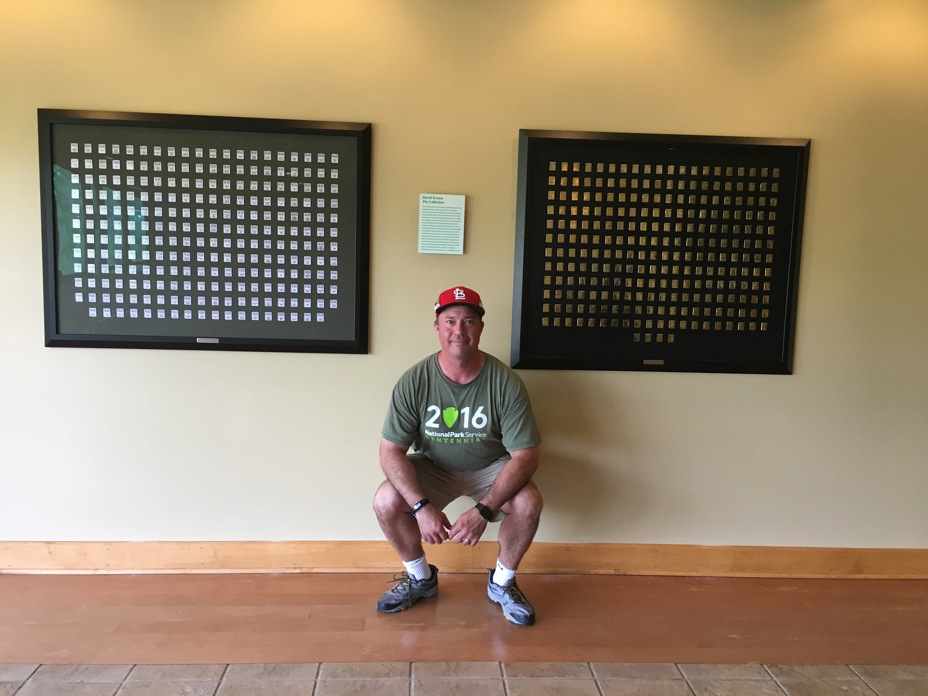 A man crouches below two framed displays of hundreds of national park collectors pins.