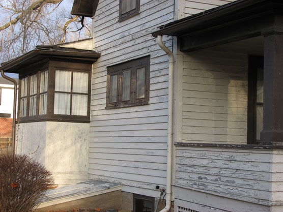 Peeling white paint on the wooden siding of a 19th century frame house.