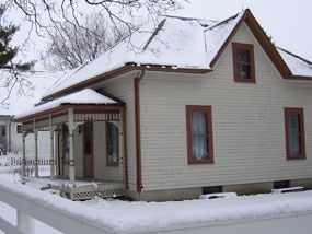 Snow covers the roof and lawn of a two-story cream colored house with brown trim. Snow covers the roof and lawn of a two-story cream colored house with brown trim.
