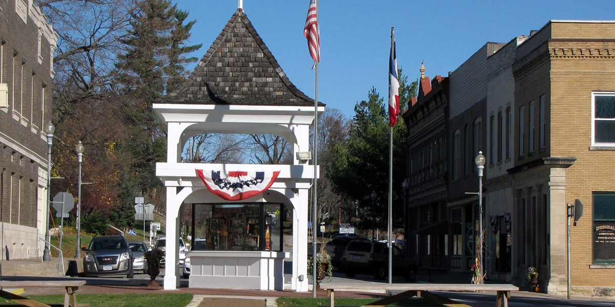 A white gazebo with flags in front of historic commercial downtown block. A white gazebo with flags in front of historic commercial downtown block.