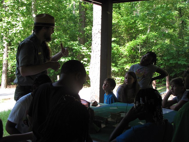 Ranger with children at a picnic table, trees in background
