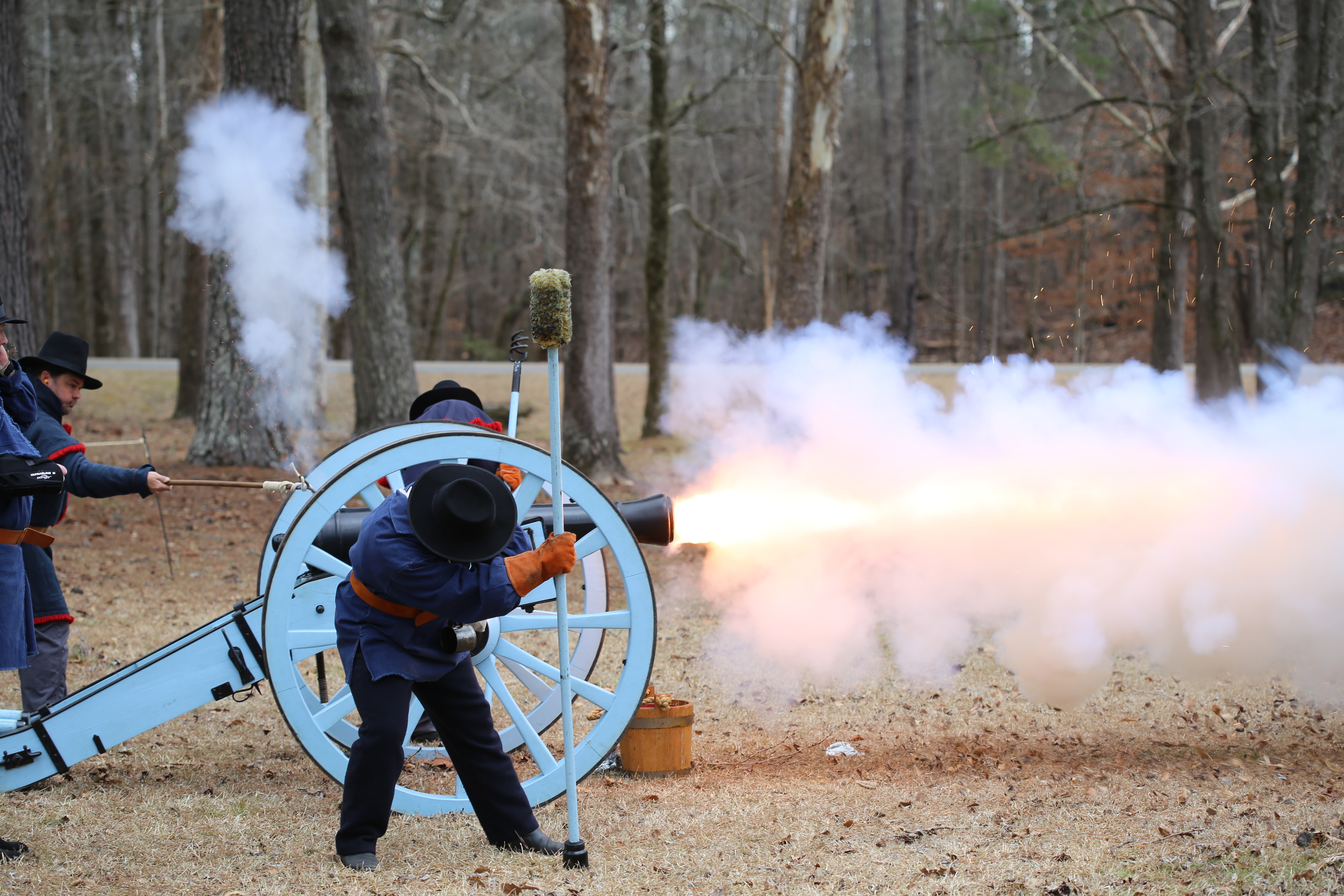 men in period uniforms shooting cannon; smoke and fire coming out of barrel