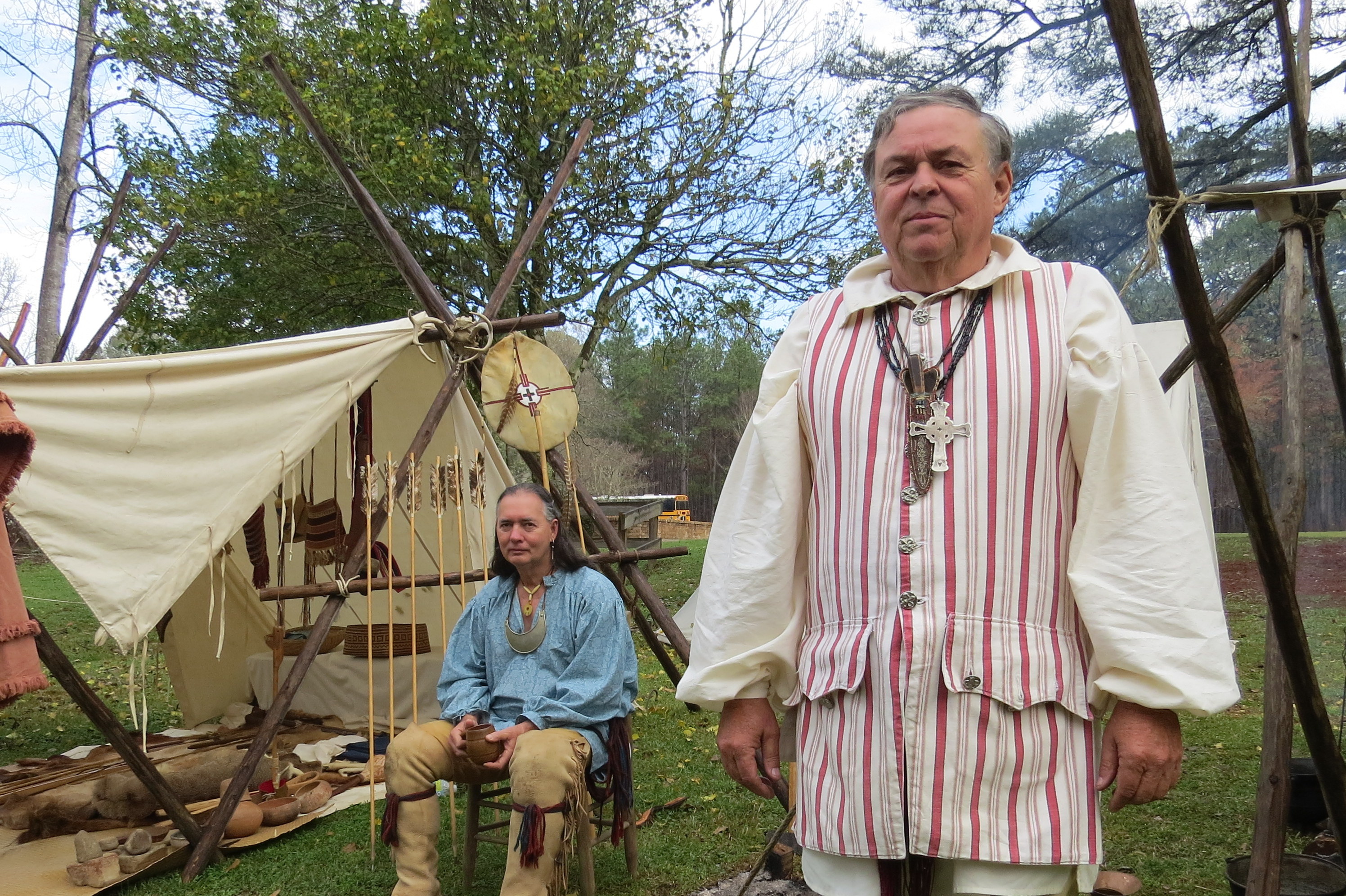 two men, one standing in foreground the other sitting in background, dressed as Creek Indians