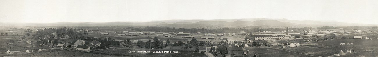 Several large buildings in the foreground with large hills in the background