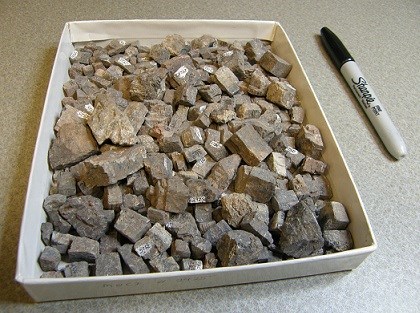 A white square box filled with small, square pieces of a gray/silver rock-shaped mineral.