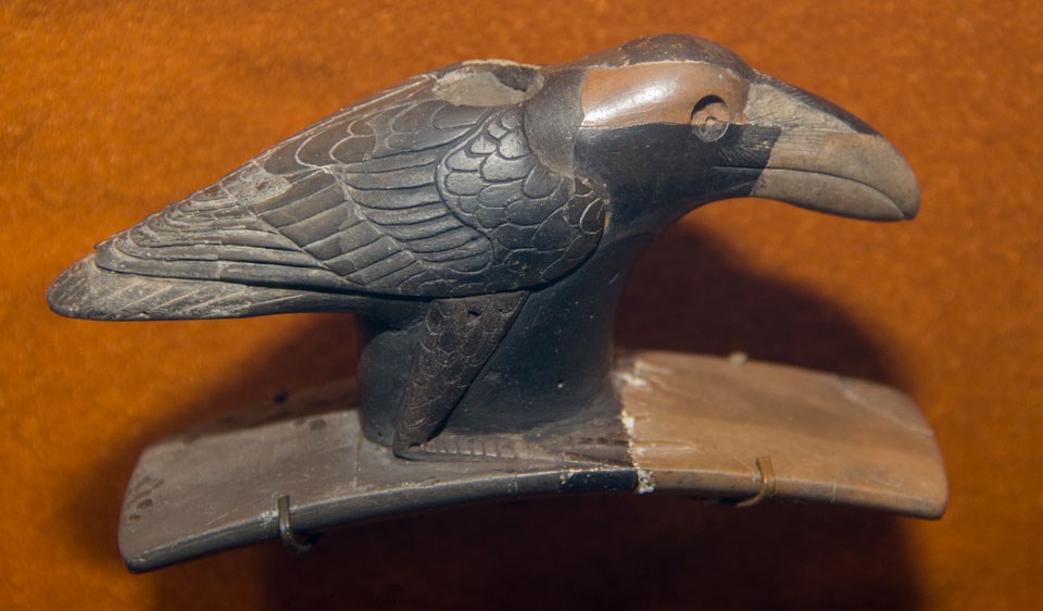 Raven Pipe A dark-colored pipe carved to resemble a bird with head to the right and tail to the left atop an upward-curved platform